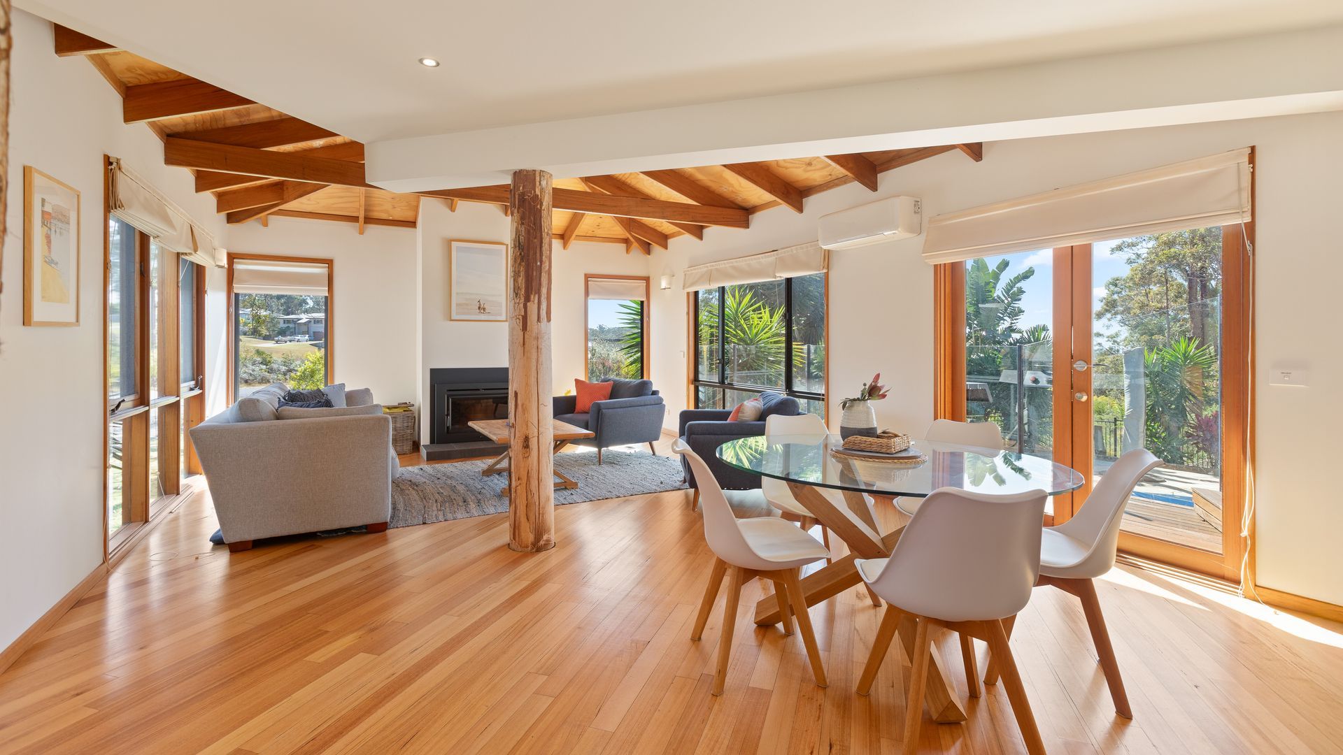 A spacious living area with a glass dining table, wooden flooring, and a fireplace.