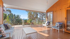 A spacious outdoor deck with wooden flooring, a white table, and two sofas with cushions.
