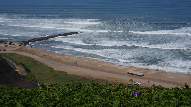 A coastal view with a rocky breakwater, beach, and a road leading to a parking area. - Beautiful turist apartment with BALCONY AND OCEAN VIEWS.  max. 8 persons. (Miraflores)