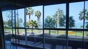 A view from inside a building with large windows overlooking a parking area with cars and palm trees. - Beautiful turist apartment with BALCONY AND OCEAN VIEWS.  max. 8 persons. (Miraflores)