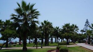 A park with palm trees, a paved walkway, and a grassy area with a heart-shaped flower bed. - Beautiful turist apartment with BALCONY AND OCEAN VIEWS.  max. 8 persons. (Miraflores)