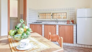 Eine Küche mit Holzschränken, einem weißen Kühlschrank, einer Spüle und einem Fenster über der Arbeitsplatte.