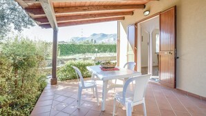 Eine überdachte Terrasse mit Tisch und Stühlen, ein Korb voller Zitronen und Blick auf ein Weinberg und Berge.