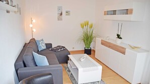 Een moderne woonkamer met een grijze bank, een witte salontafel en een kleine zwarte fauteuil. Op de salontafel staat een plant en in de hoek een lamp.