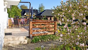 Een terras met buitenmeubilair, een houten poort en een tuin vol bloeiende bloemen.