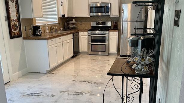 A kitchen with white cabinets, a stainless steel oven, and a marble floor. - Spacious North Houston Getaway rental (Tomball)