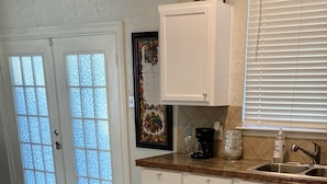 A kitchen with white cabinets, a marble floor, a coffee maker, and a window with blinds. - Spacious North Houston Getaway rental (Tomball)