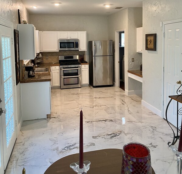 A modern kitchen with white cabinets, stainless steel appliances, and a marble floor.
