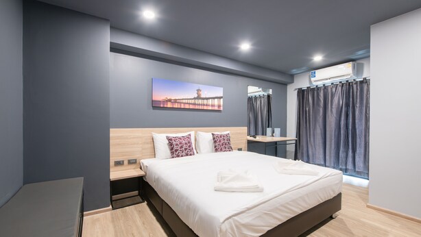 Una habitación de hotel moderna con una cama grande, una mesita de noche, un escritorio y una ventana con cortinas.