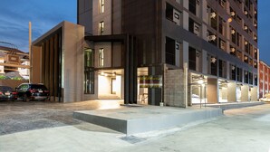 Un hotel moderno de varios pisos con una entrada destacada, ventanas amplias y un área de estacionamiento.