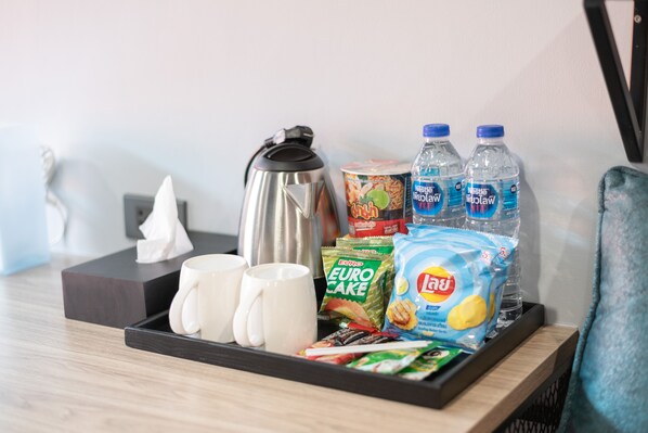 A tray with a kettle, two bottles of water, a can of fruit, a pack of Euro cake, and a pack of Lay's chips. - Oblique Apartment (Bang Yai)