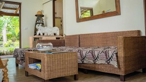 Ein Zimmer mit einem Korbssessel, einem kleinen Tisch mit einer Schale, einem dekorativen Hut und einem Spiegel an der Wand.