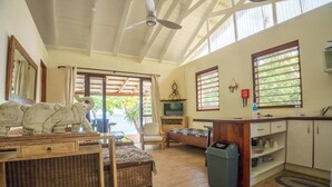 Ein geräumiges Zimmer mit Deckenventilator, Fernseher, Sofa, Esstisch und Küchenzeile.