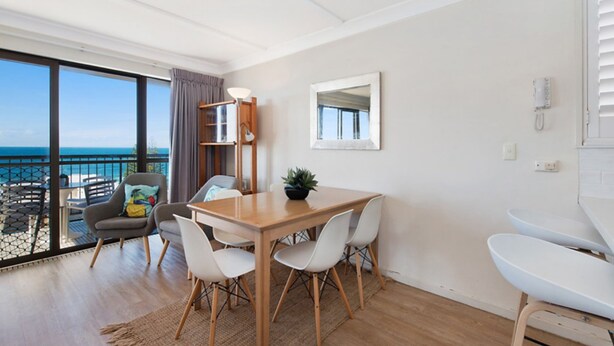 A modern room with a wooden dining table, white chairs, a potted plant, and a view of the ocean through large windows. - Oceanic Apartments Unit 13 Stunning Ocean Views (Kings Beach)