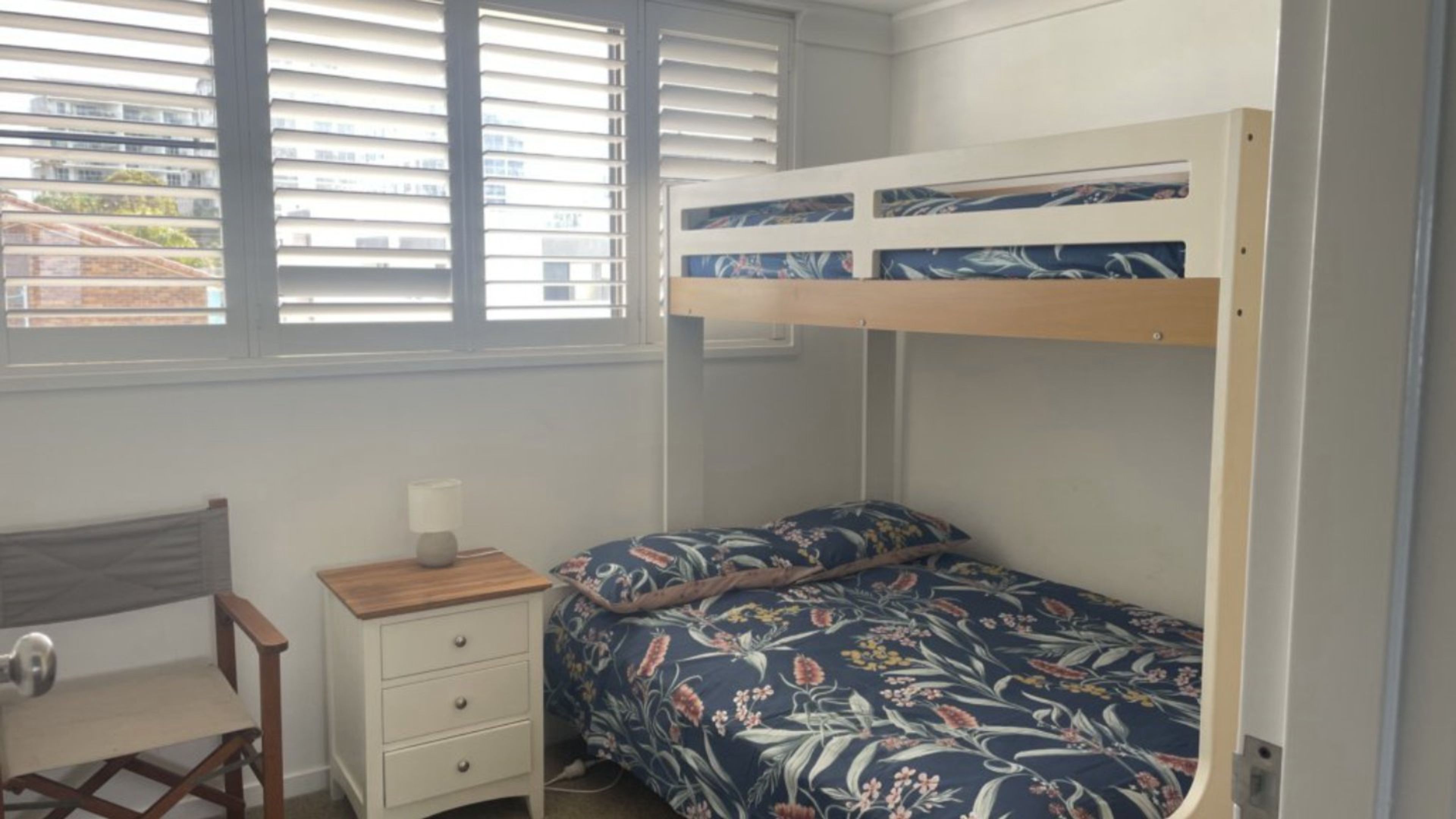 A bunk bed with a floral bedspread, a bedside table with a lamp, and a chair.