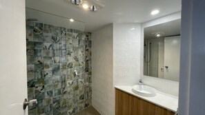 Un baño con pared de ducha enlosada, un lavamanos con espejo y armarios de madera.