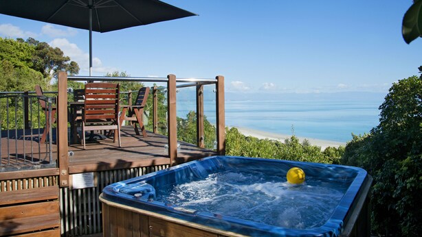 A wooden deck with a hot tub, chairs, and an umbrella overlooking a beach.