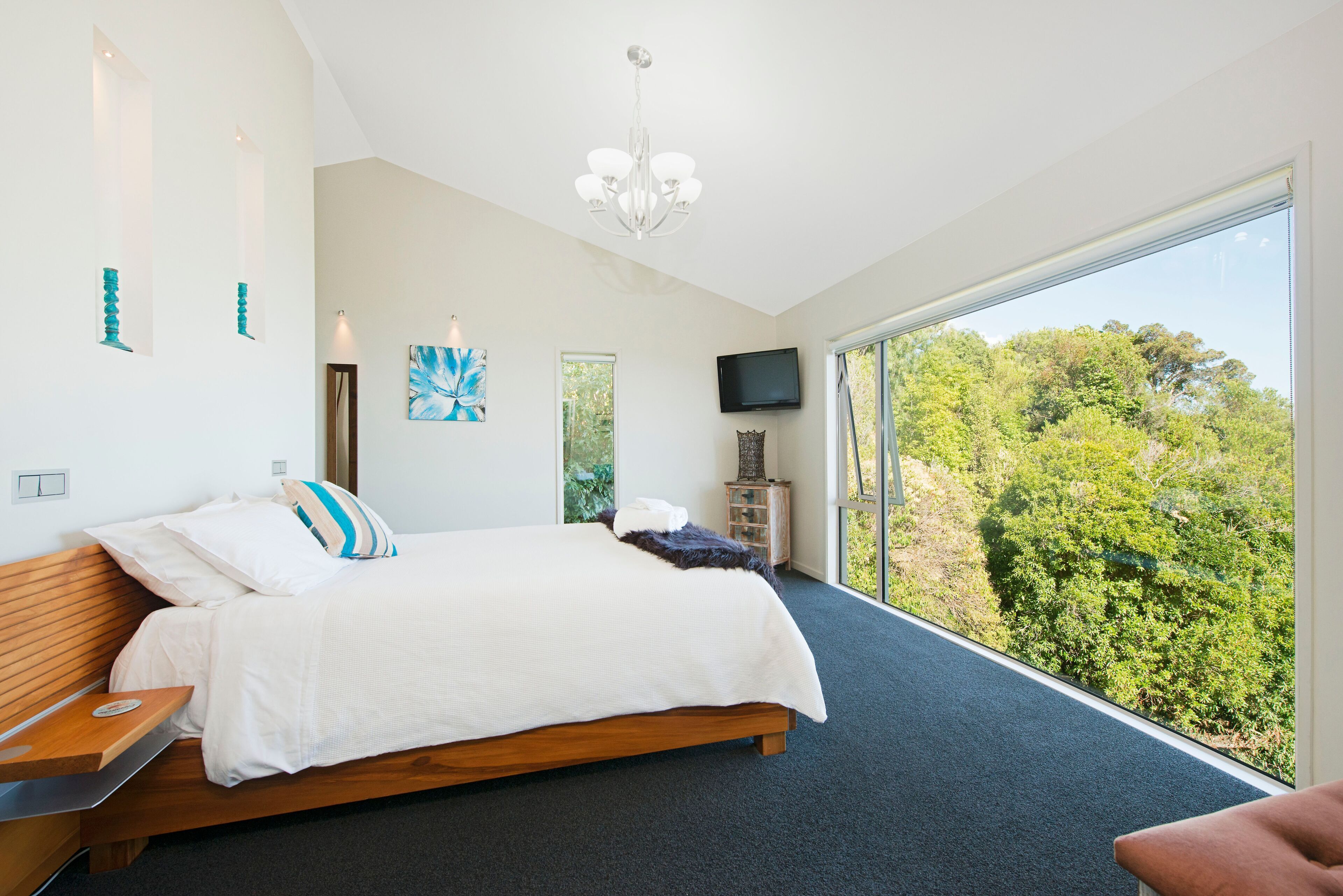 A modern bedroom with a large bed, a TV, and a view of trees.