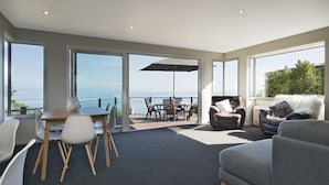 A modern living room with a view of the sea, a balcony with a table and chairs, and a large window.