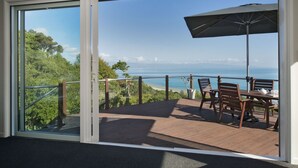 A deck with a table and chairs, overlooking a scenic view of the ocean and greenery.