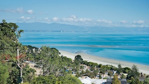 A coastal view with a beach, clear blue waters, and a mountainous backdrop.