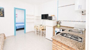 A compact kitchen with a gas stove, microwave, and a sink. There is a dining area with a table and chairs, and a small refrigerator. - Apartamento cerca de la playa de Conil (Conil de la Frontera)