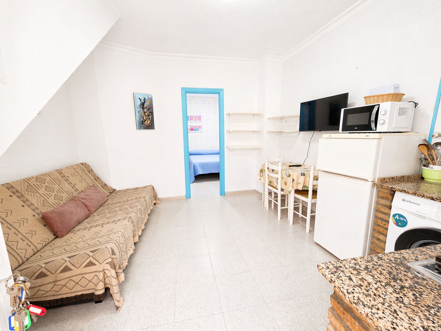 A room with a bed, a small table, a microwave, and a washing machine.