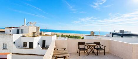 Terraza en la azotea con mesa y sillas, con vistas a la playa.