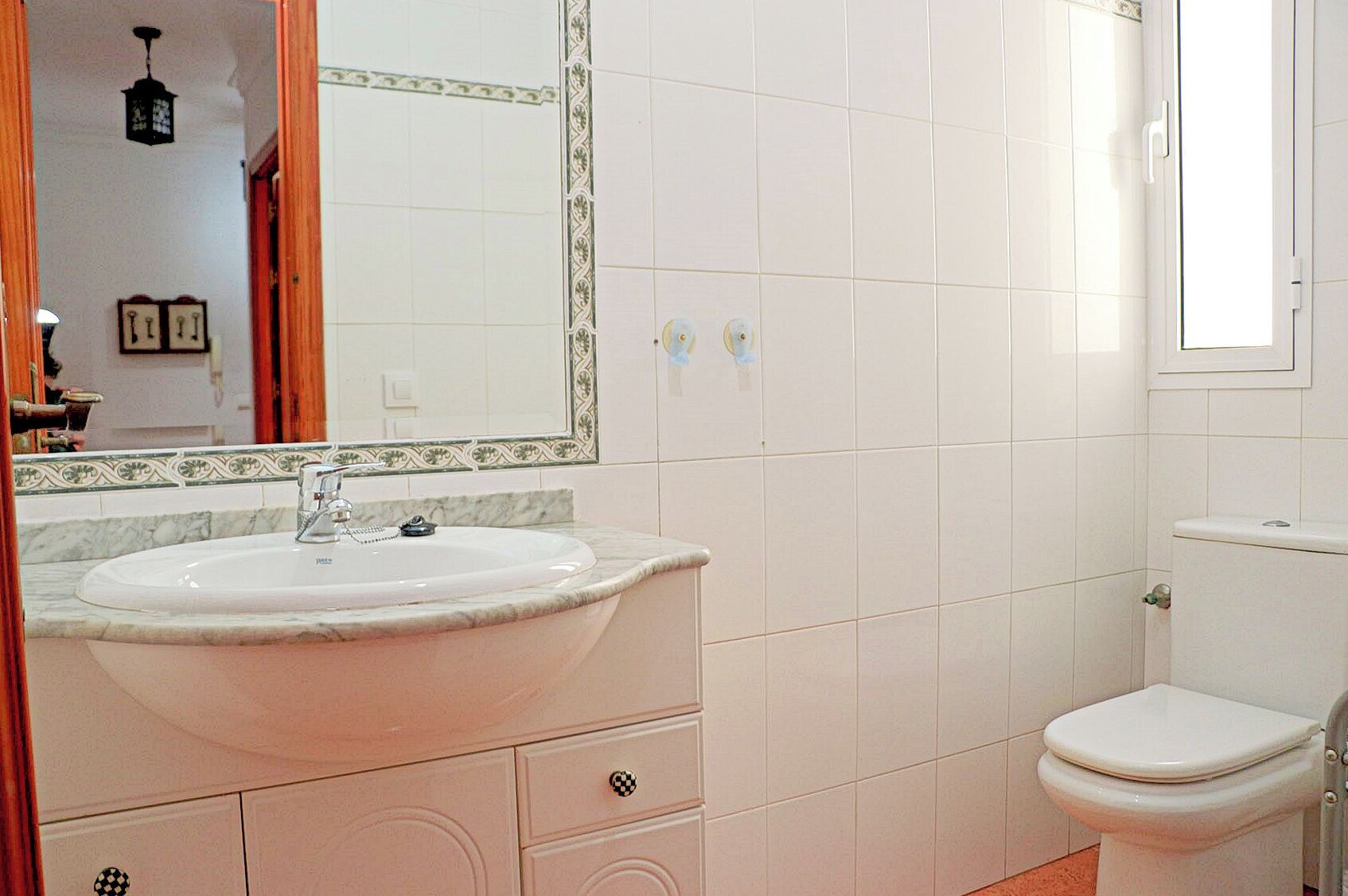 A bathroom with a white sink, a toilet, and a mirror with a decorative frame.