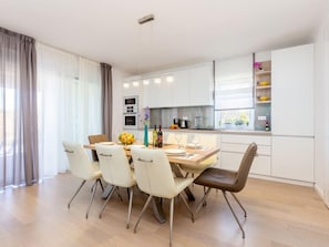 Une cuisine moderne avec des meubles blancs, une table à manger avec des chaises et un îlot de cuisine.