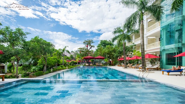 A swimming pool with red umbrellas, lounge chairs, and a building with balconies. - Chez Carole Center Resort & Spa (Phu Quoc)