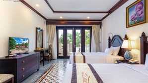 A hotel room with two beds, a desk, a television, and a view of the outdoors through a glass door. - Chez Carole Center Resort & Spa (Phu Quoc)