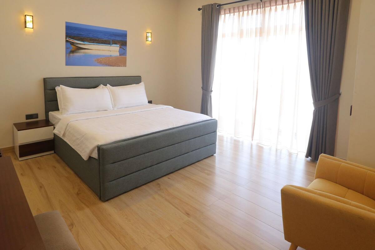 Een moderne slaapkamer met een groot bed, een nachtkastje, een stoel en een schilderij aan de muur.
