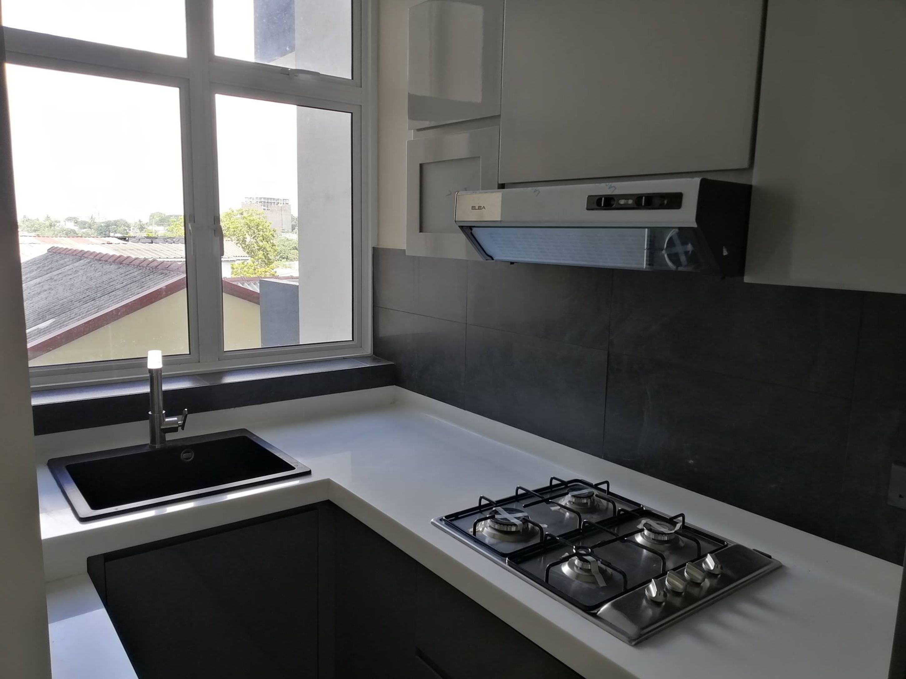 A modern kitchen with a gas stove, a sink, and a window overlooking a residential area.