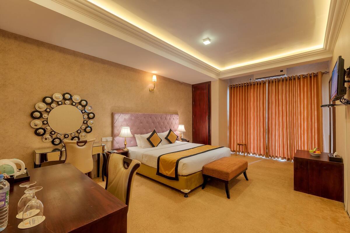 A hotel room with a large bed, a round mirror, a desk, and a television.