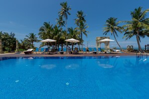 A clear blue pool with lounge chairs and umbrellas, surrounded by palm trees and a stone archway. - Seagate Hotel (Kalutara)