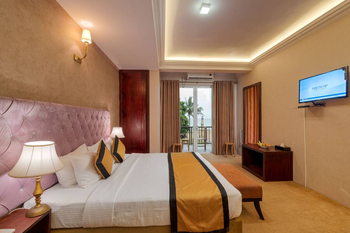 A hotel room with a large bed, a TV, a desk, and a view of the outdoors.