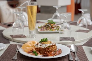 A dining table with a plate of food, a glass of beer, and a glass of water. - Seagate Hotel (Kalutara)