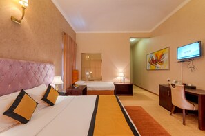 A hotel room with a large bed, a desk, a television, and a bathroom mirror.