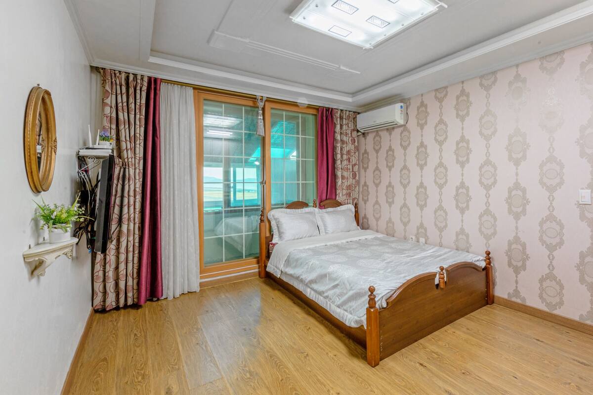 A bedroom with a wooden bed, a sliding glass door to a balcony, a large mirror, and patterned wallpaper.
