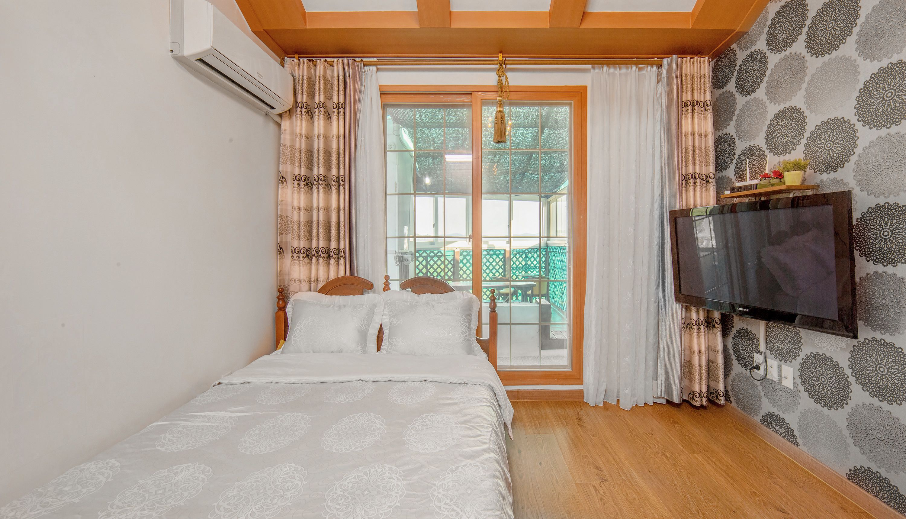 A bedroom with a bed, a TV mounted on the wall, and a window with curtains.