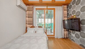 Ein Schlafzimmer mit einem Bett, einem an der Wand montierten Fernseher und einem Fenster mit Vorhängen.