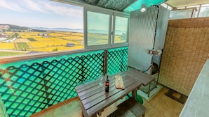 A balcony with a view of agricultural fields, a table with a bottle and glass, and a metal railing. - Goorm Dari Pension (Incheon)