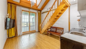 A spacious room with a wooden staircase, a bench, a kitchen area, and large windows with curtains. - Goorm Dari Pension (Incheon)