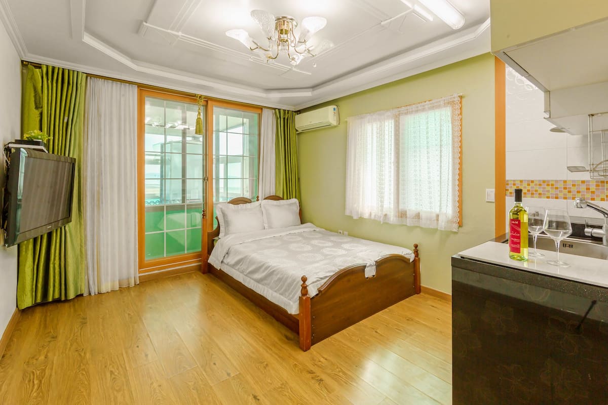 A hotel room with a bed, a TV, a window with curtains, a sink, and a mirror.