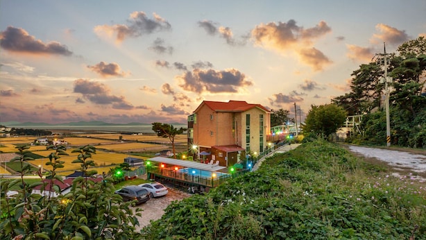 A hotel with a red roof, a covered outdoor seating area, and a view of the surrounding landscape. - Goorm Dari Pension (Incheon)