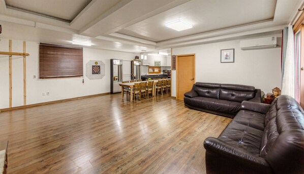 Ein geräumiges Wohnzimmer mit Holzboden, einer Ledersofa, einem Esstisch mit Stühlen und einer Küchenzeile mit Schränken und Geräten.