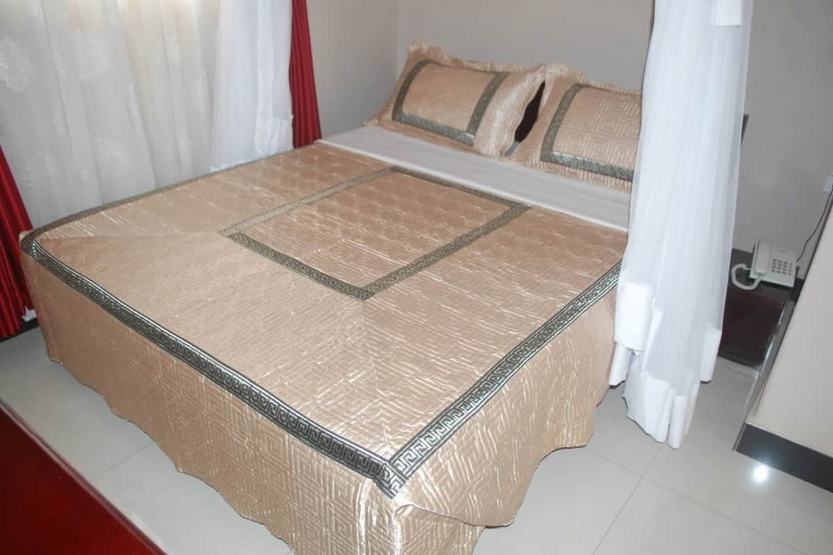 A bed with a patterned bedspread, a telephone, and a curtain.
