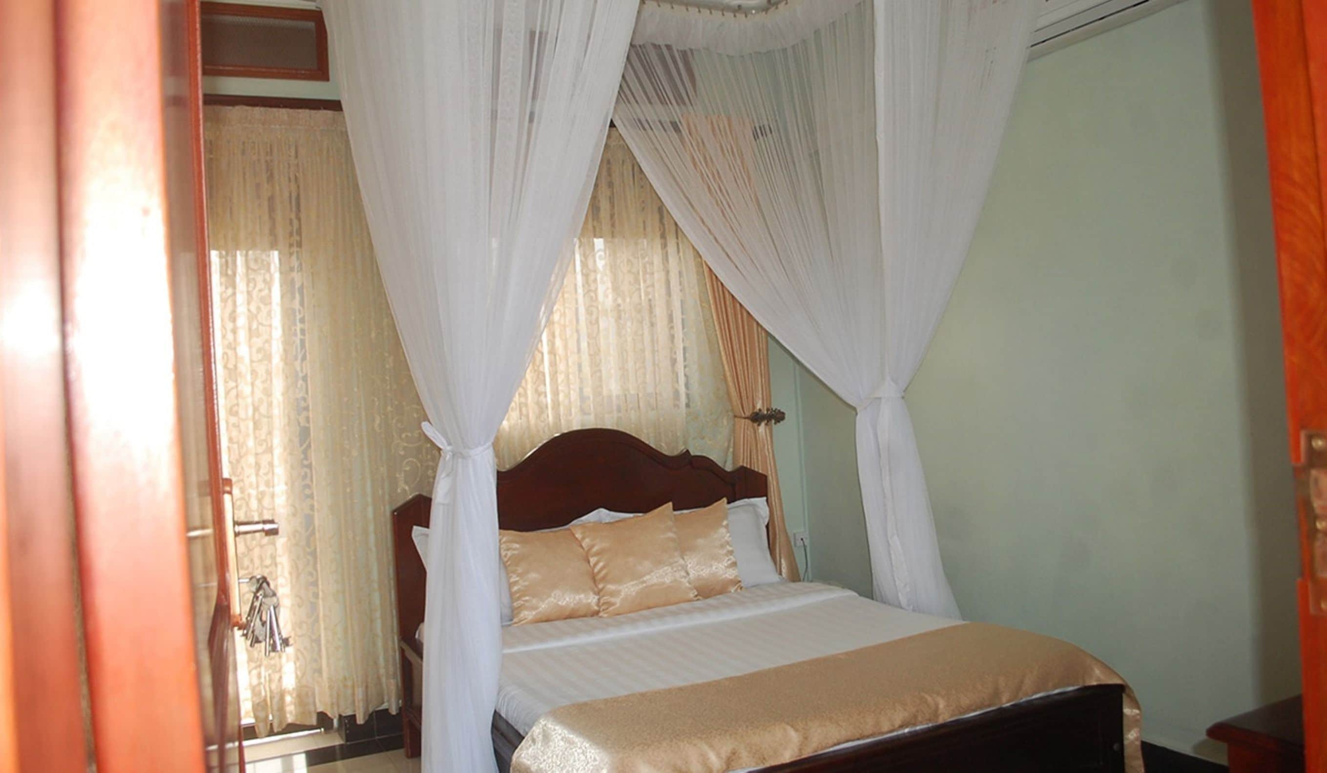A bedroom with a bed, white curtains, and a wooden headboard.
