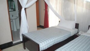 Ein Schlafzimmer mit zwei Betten und einem durchgehenden Türrahmen erkennbaren Badezimmer. Ein roter Vorhang ist zu sehen.